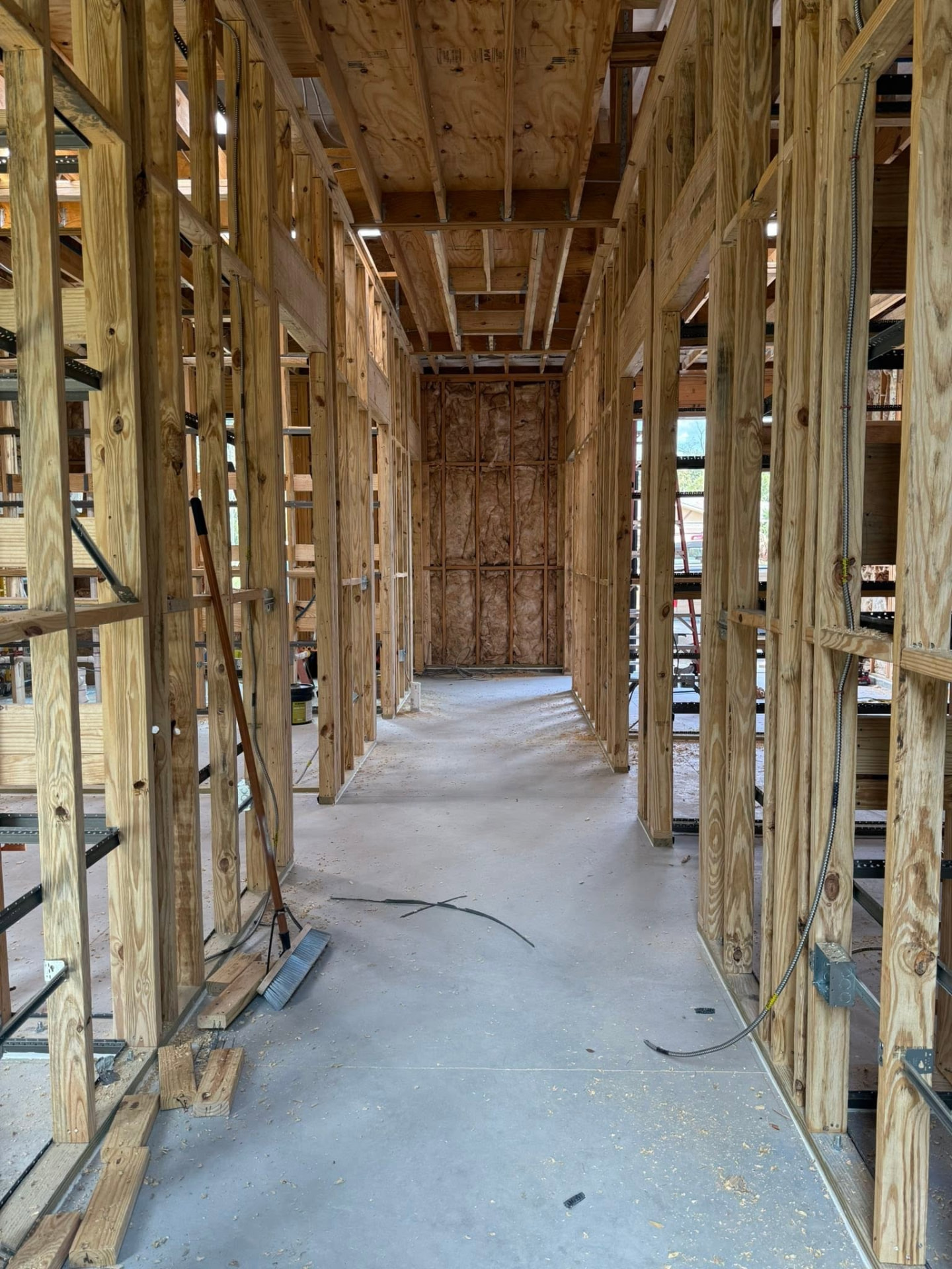 Urology clinic corridor during rough framing — wood studs, open ceiling joists, and unfinished slab